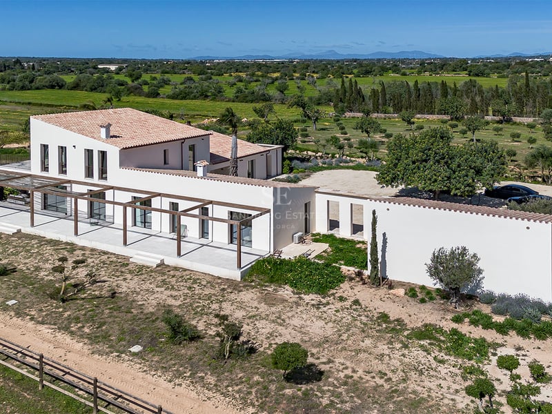 Vue aérienne d'une villa blanche méditerranéenne avec pergolas en bois entourée de verdure.