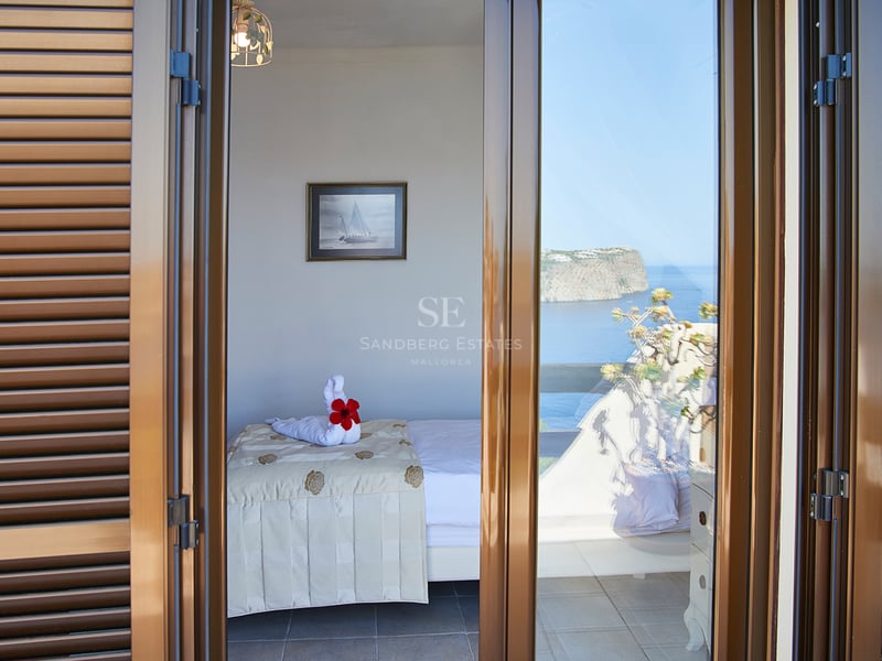 Chambre vue à travers des volets ouverts avec lit simple, cygne en serviette et vue sur la mer et les falaises.