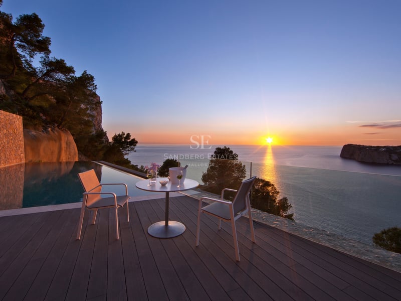 Coucher de soleil depuis une terrasse de luxe avec piscine à débordement et mobilier moderne blanc.