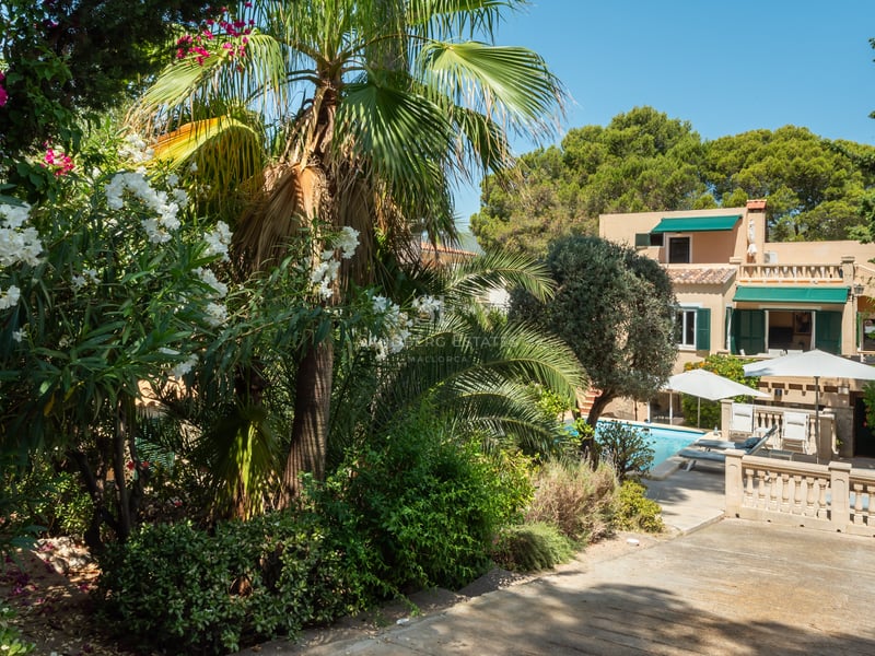 Vue d'une villa ocre classique entourée d'une végétation méditerranéenne dense, de palmiers et d'une piscine bleue.