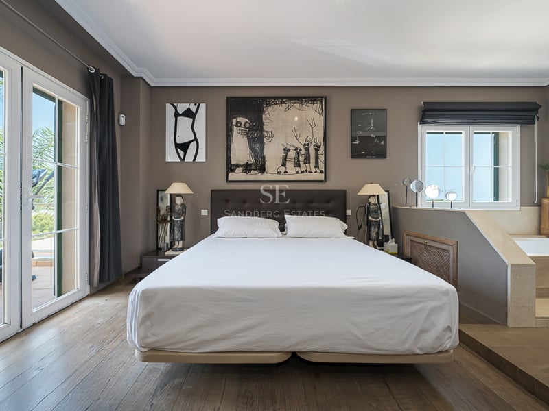 Chambre moderne avec lit double, parquet en bois et jacuzzi intégré à côté des portes-fenêtres.