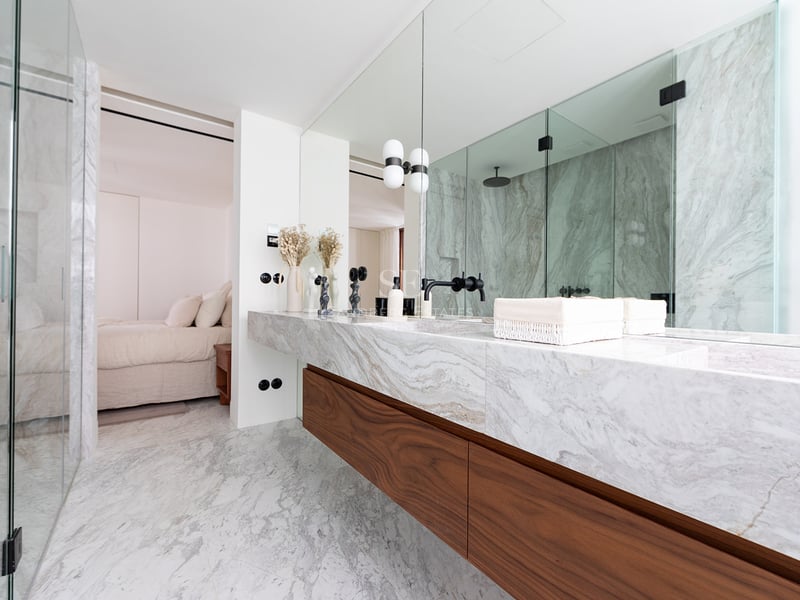 Baño moderno con lavabo doble de mármol, muebles de nogal y ducha de vidrio integrada.