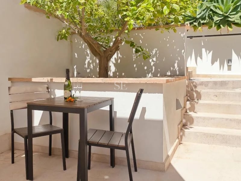 Petite table de bistrot en bois et deux chaises sur un patio en pierre ensoleillé à côté d'un citronnier.