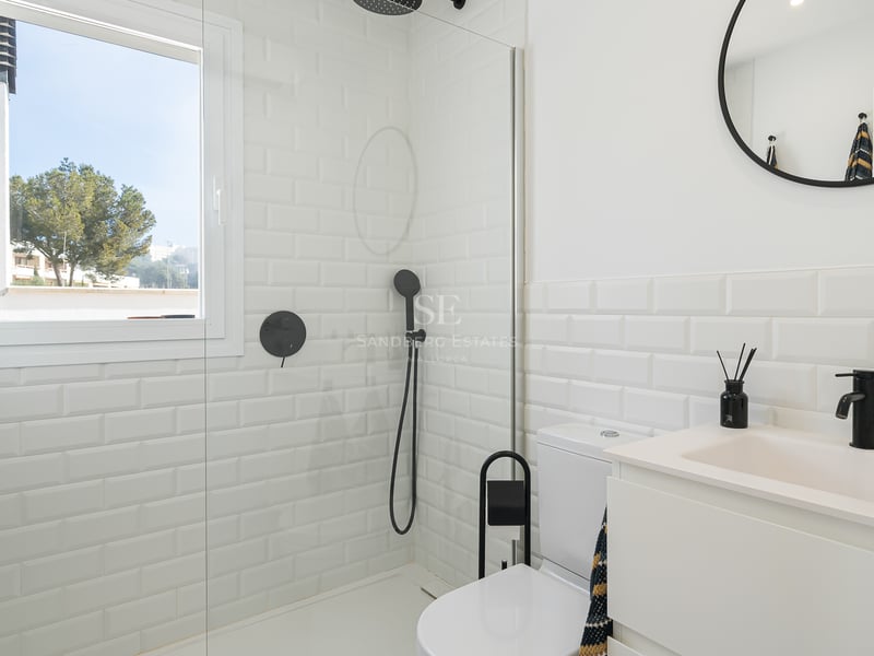 Salle de bain lumineuse avec carrelage métro blanc, paroi de douche en verre et robinetterie noire mate.