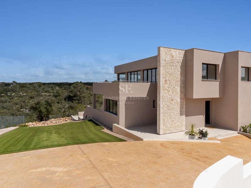 Villa moderne de deux étages avec façade sable, accents en pierre naturelle et grandes baies vitrées sur la pelouse.