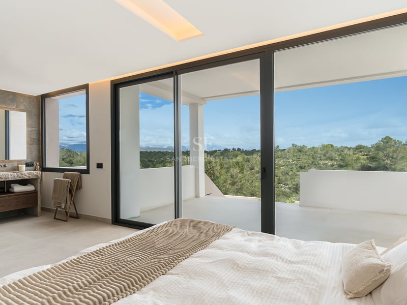 Chambre principale avec grandes baies vitrées coulissantes ouvrant sur une terrasse privée avec vue sur les collines.