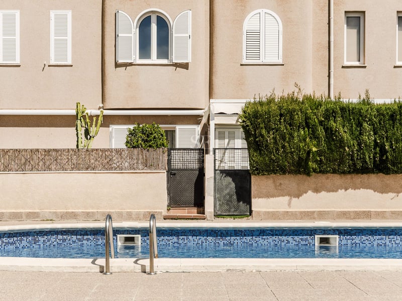 Piscine extérieure en mosaïque bleue devant une façade beige aux volets blancs.