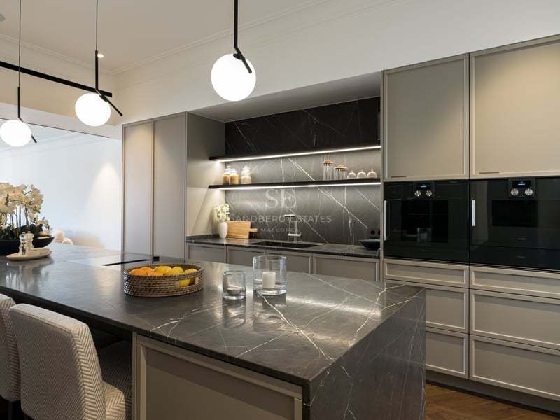 Modern kitchen featuring a dark marble island with seating, grey cabinetry, integrated appliances, and spherical pendant lights.