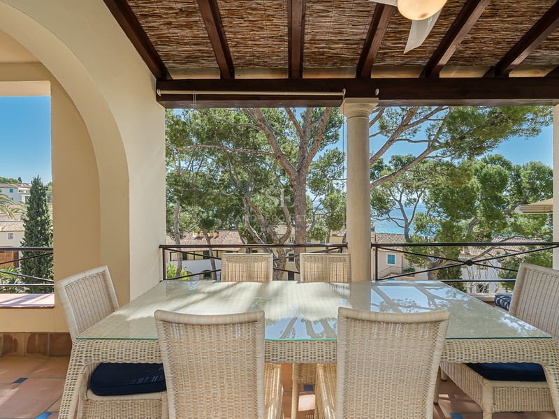 Terrasse couverte avec salle à manger en osier, sol en terre cuite et vue sur les pins et la mer.