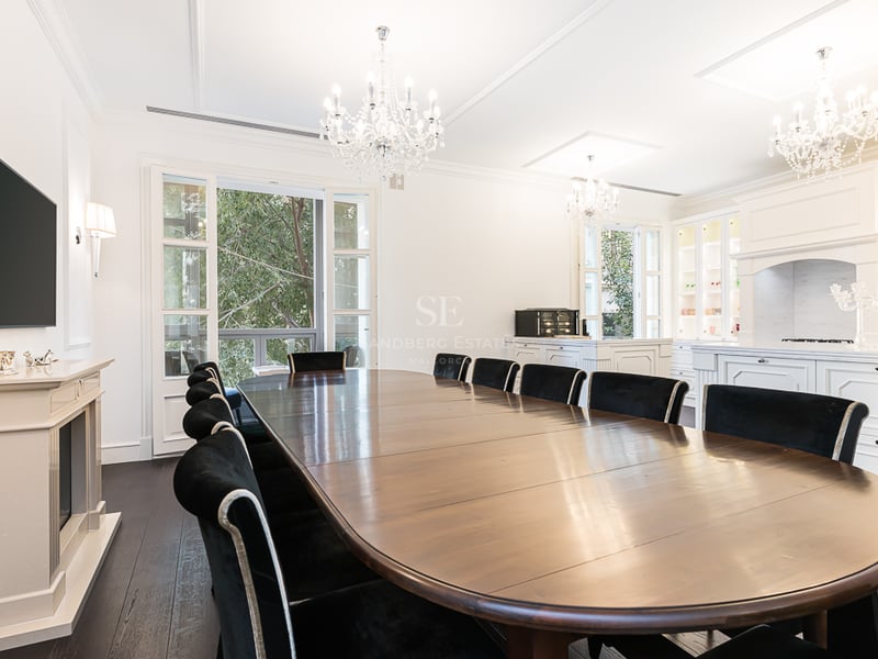 Grande table à manger en bois et chaises en velours noir sous des lustres en cristal dans une pièce blanche lumineuse.