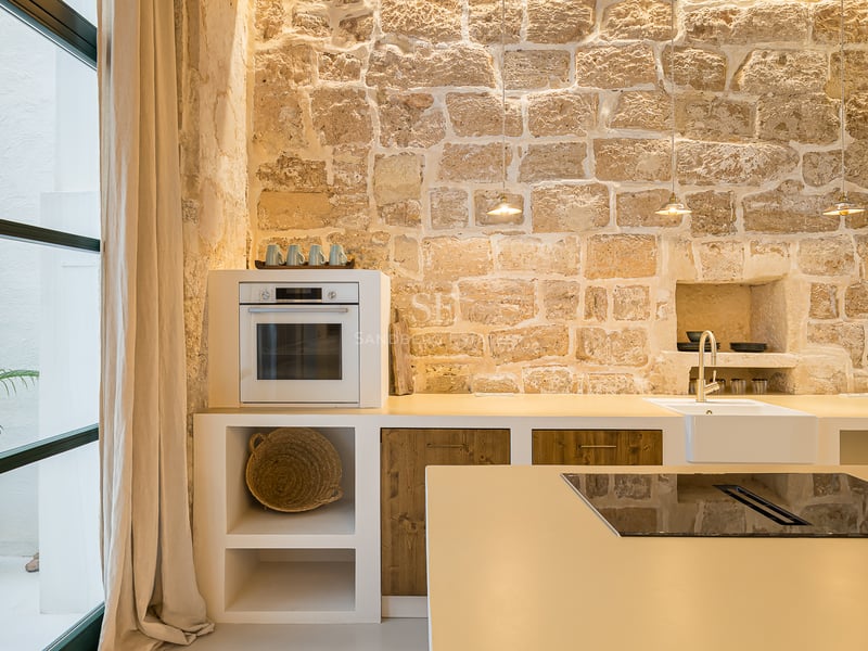 Cuisine moderne avec un grand mur en pierre apparente, des armoires blanches, des accents en bois et des appareils intégrés.