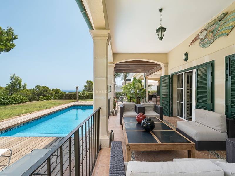 Porche couvert avec salon de jardin donnant sur une piscine, une terrasse en bois et la mer au loin.