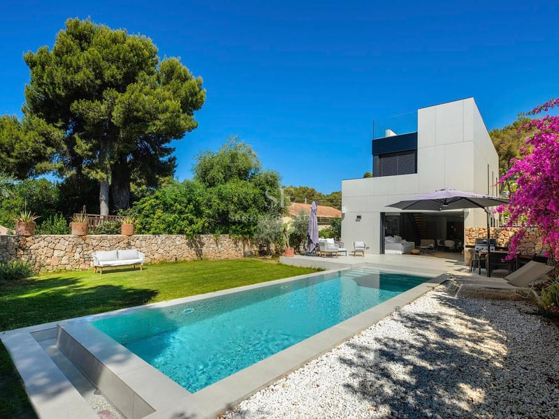 Piscine rectangulaire entourée d'une pelouse, de gravier blanc et d'une villa blanche moderne sous un ciel bleu.
