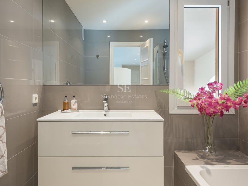Salle de bains contemporaine avec meuble vasque blanc, grand miroir et carrelage taupe avec accents chromés.