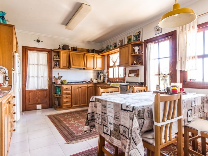 Cuisine rustique lumineuse avec des armoires en bois, une table à manger avec nappe et de la lumière naturelle.