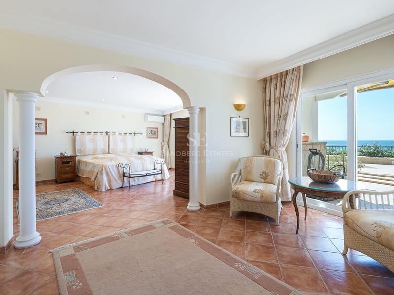 Chambre de style méditerranéen avec sol en terre cuite, colonnes classiques et portes vitrées ouvrant sur la mer.