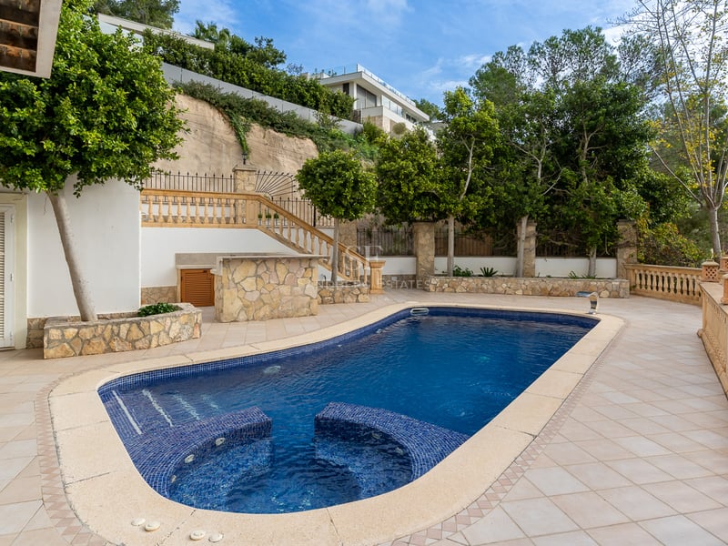 Piscine bleue avec sièges intégrés sur une terrasse carrelée entourée de balustrades et d'arbres.