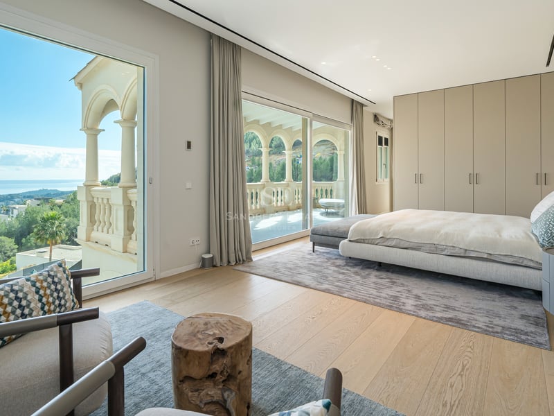 Chambre de maître moderne avec baies vitrées, parquet en chêne clair et balcon privé surplombant la côte.