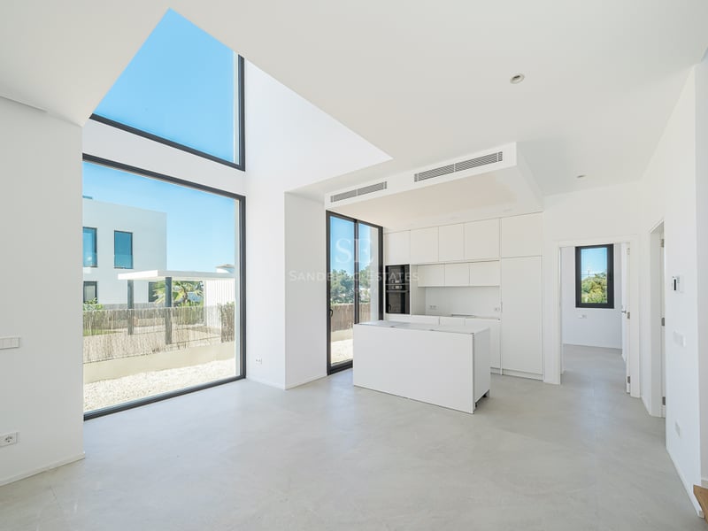 Cuisine blanche minimaliste avec îlot, baies vitrées double hauteur et lumière naturelle abondante.