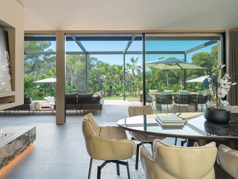 Salle à manger moderne avec table en marbre et cheminée, ouvrant sur une terrasse et un jardin luxuriant.