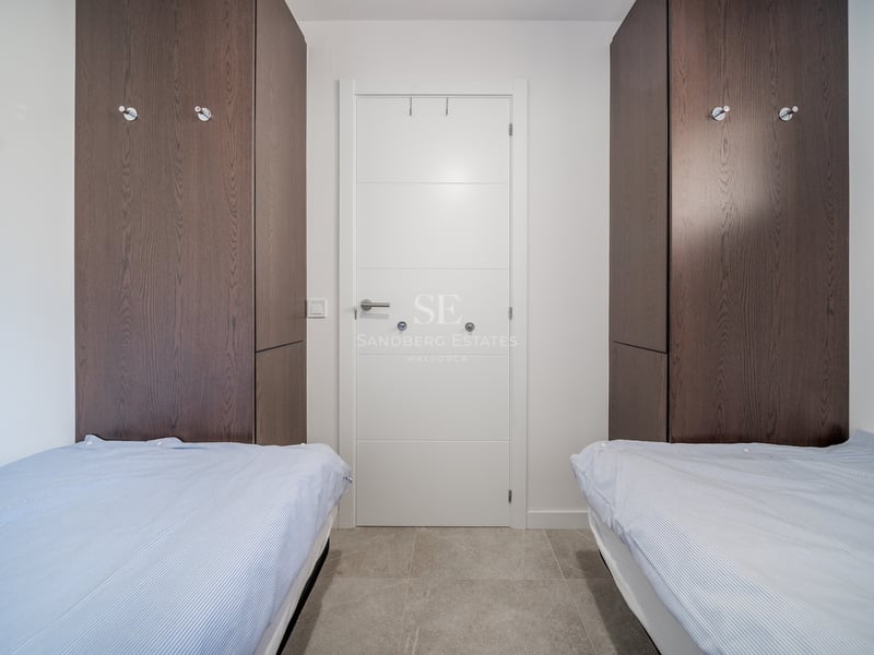 Chambre contemporaine avec lits jumeaux, placards en bois sombre et sol en carrelage gris.