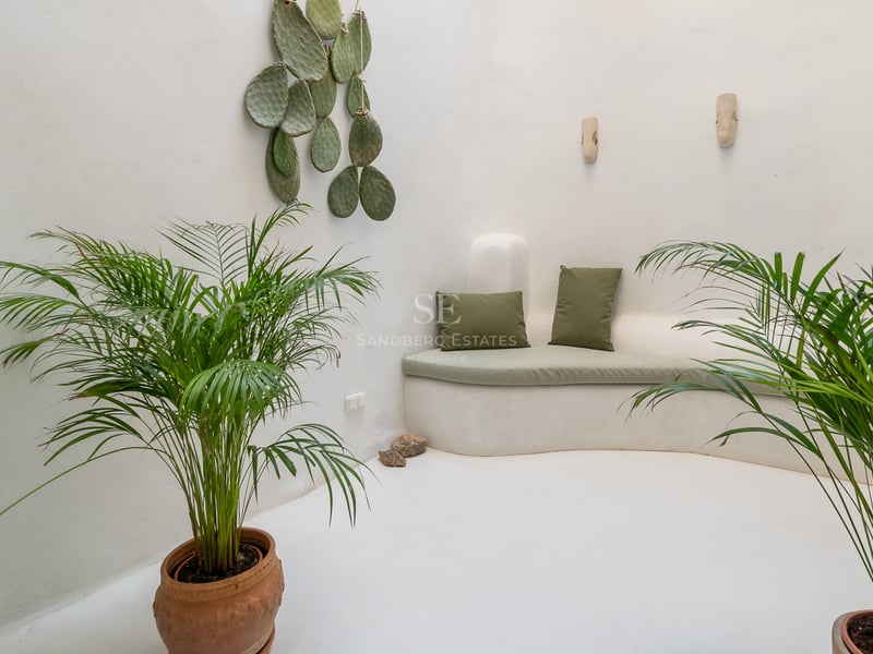 Salon minimaliste blanc avec banquette intégrée incurvée, coussins vert sauge et plantes d'intérieur.