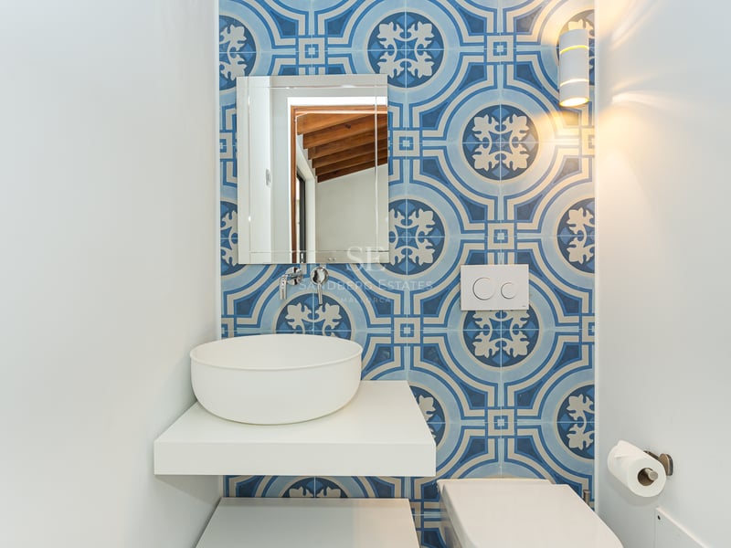 Salle d'eau avec carrelage bleu à motifs, vasque blanche sur étagère flottante et miroir rectangulaire.