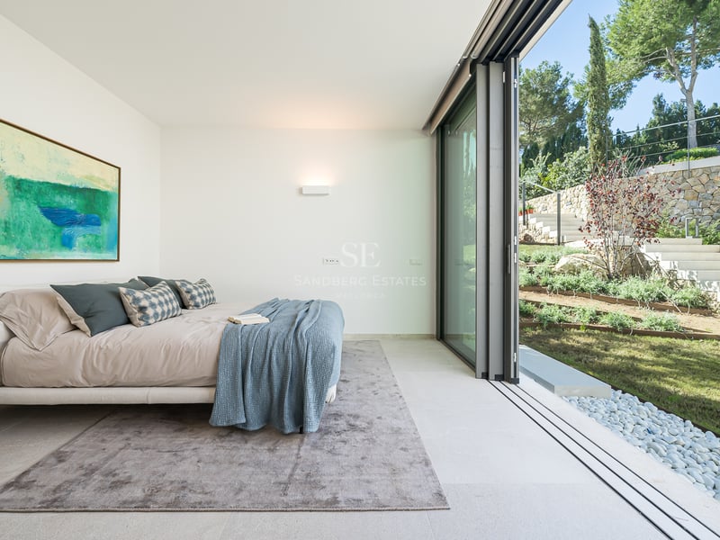 Chambre moderne avec baies vitrées donnant sur un jardin paysager avec escaliers en pierre et pelouse.