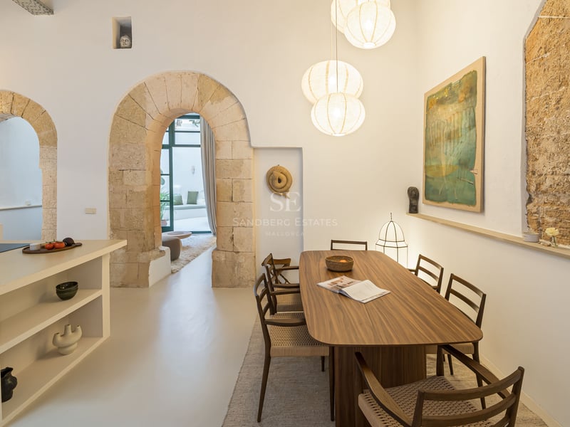 Salle à manger contemporaine avec table en bois sous des suspensions globes, encadrée par des arches en pierre.