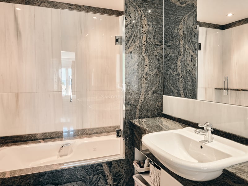 Salle de bain de luxe avec plan de toilette en granit foncé, lavabo blanc et baignoire avec paroi en verre.
