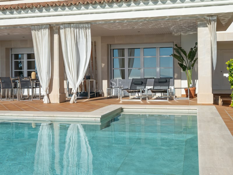 Terrasse en terre cuite avec piscine, rideaux blancs, chaises longues et coin repas extérieur abrité.