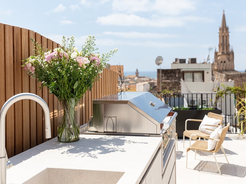 Terraza moderna con barbacoa de acero inoxidable, encimera de piedra y vistas a la catedral bajo un cielo despejado.