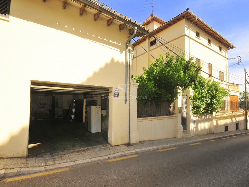 Exteriör av en beige byggnad i traditionell stil med ett öppet garage och tegeltak under en klar himmel.