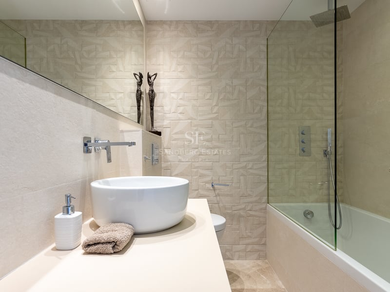 Baño moderno con lavabo sobre encimera, espejo amplio y pared de azulejos geométricos en la zona de ducha.