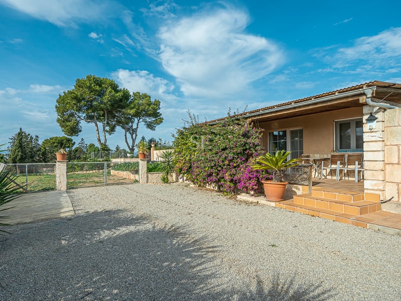 Stenfasad på en villa med terracottaporch, grusplan och bougainvillea under en klarblå himmel.