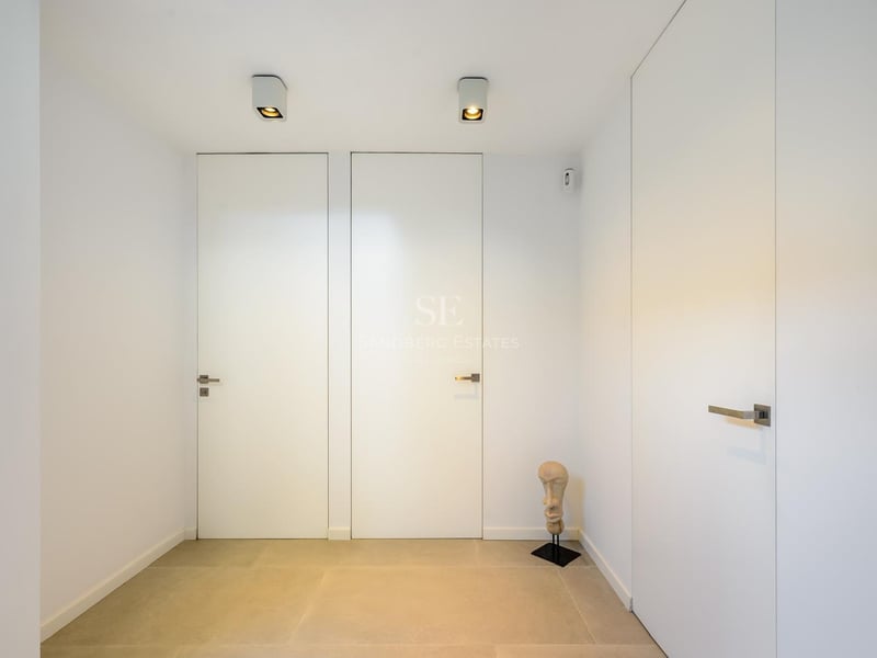 Couloir minimaliste avec portes blanches affleurantes, sol en pierre claire et petite sculpture décorative.