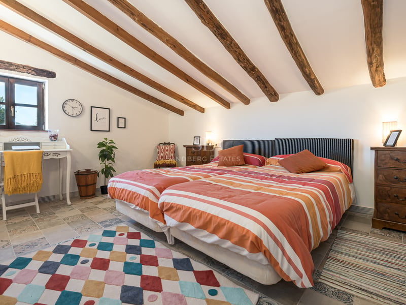 Chambre sous les combles avec poutres en bois, lits jumeaux et revêtement de sol en pierre naturelle.