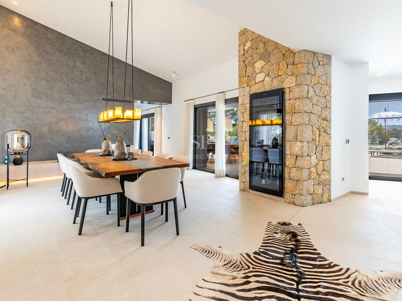 Vue extérieure d'une villa moderne avec piscine à débordement, grandes fenêtres et design minimaliste. Pelouse soignée et ciel dégagé.