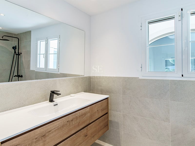Intérieur d'une salle de bain moderne avec meuble en bois, lavabo blanc, robinetterie noire et carrelage gris.