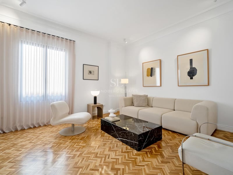 Salon lumineux avec murs blancs, parquet en chevrons, canapé beige et table basse en marbre noir.