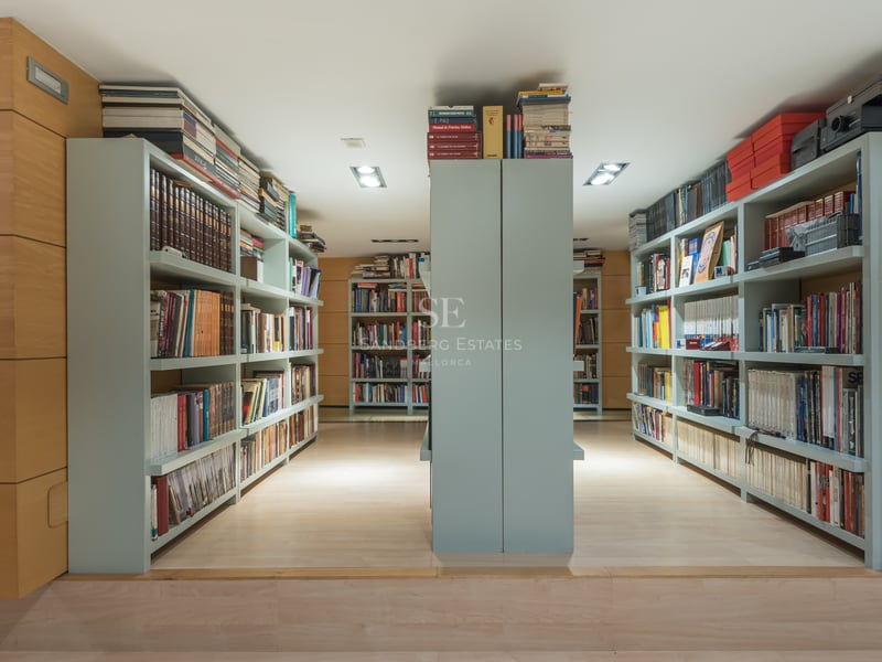 Modern home library with light oak wood paneling and extensive built-in sage green bookshelves.