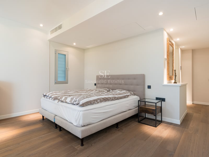 Chambre contemporaine avec lit double, tête de lit taupe, parquet en chêne et éclairage encastré chaleureux.