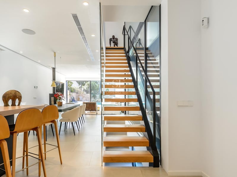 Intérieur moderne montrant un escalier suspendu en bois, un garde-corps en verre et un salon lumineux.