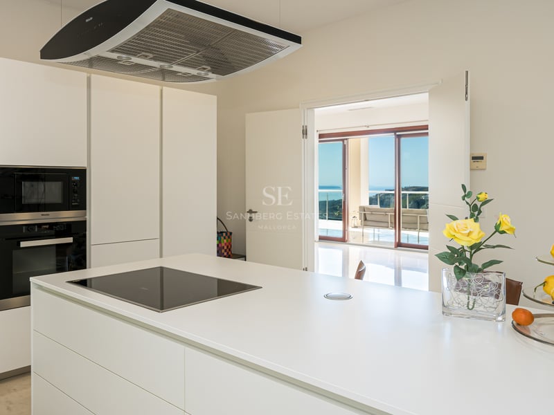 Cuisine moderne blanche et lumineuse avec îlot central, appareils Miele intégrés et vue sur la terrasse et la mer.