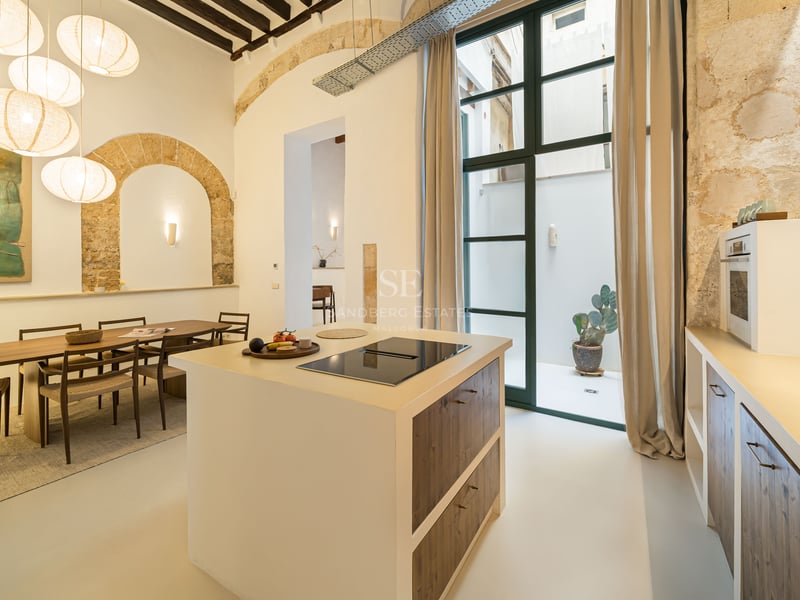 Cuisine moderne avec îlot, table à manger, suspensions boules en papier et arches en pierre apparente.