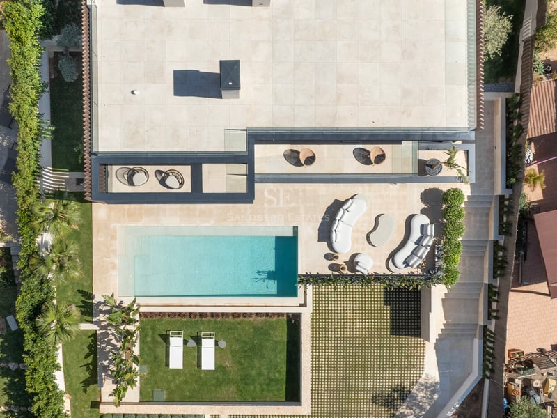 Vue plongeante d'une villa moderne avec piscine, transats, salon extérieur et jardins paysagers.