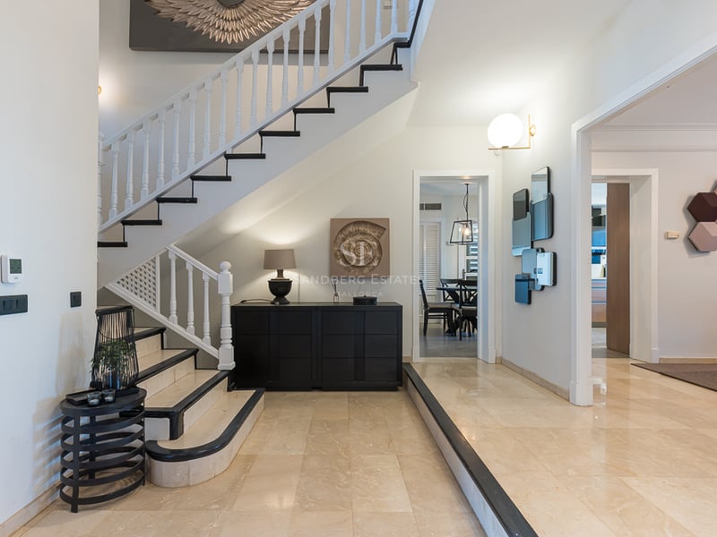 Vue intérieure d'un hall d'entrée de luxe avec sol en marbre beige, escalier blanc et noir et art moderne.