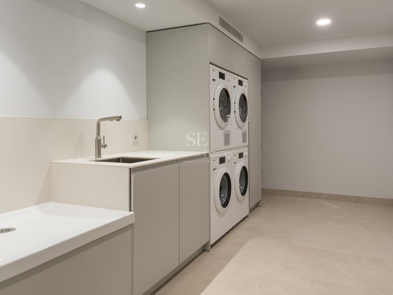 Buanderie moderne équipée de lave-linge et sèche-linge Miele, rangements épurés et grand bac de lavage.