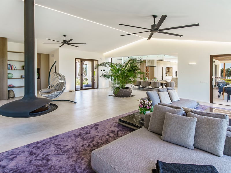 Salon contemporain avec un grand canapé gris, un tapis violet texturé et deux ventilateurs de plafond industriels.
