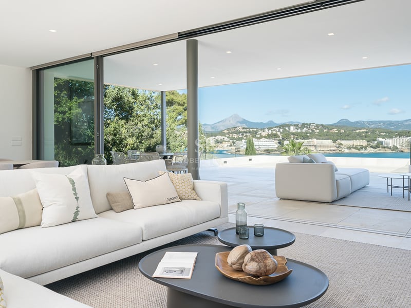 Salon lumineux avec canapés blancs s'ouvrant sur une terrasse avec une vue imprenable sur l'océan et la montagne.
